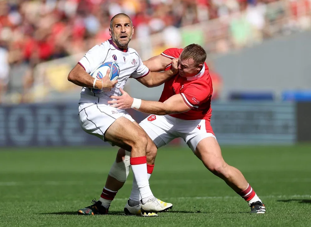 Lasha Khmaladze holding a rugby ball while grappling with another player